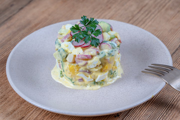 Delicious salad with cucumber, radish and egg with cream sauce in a plate on wooden background. Healthy food, close up