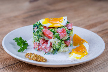Delicious salad with broccoli, tomato, onion and boiled egg with cream sauce in plate on wooden background. Healthy food