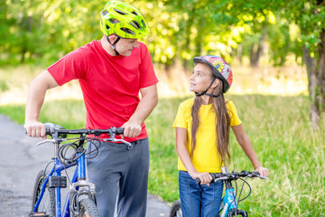 Obraz premium Father and his daughter are cycling in the summer park together