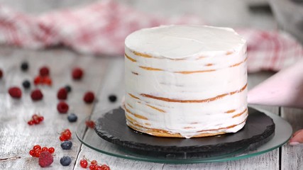 Pastry chef piping out cream filling on to a sponge cake layer.