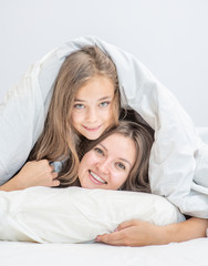 Mom and daughter have fun on the bed under blanket