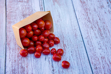 Organic ripe cherry tomatoes in a recyclable paper box on a wooden table. Cooking ingredients. Harvest. Sustainable living. Say “no” to plastic packaging.
