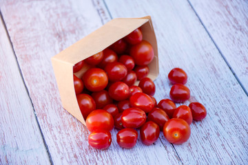 Organic ripe cherry tomatoes in a recyclable paper box on a wooden table. Cooking ingredients. Harvest. Sustainable living. Say “no” to plastic packaging.