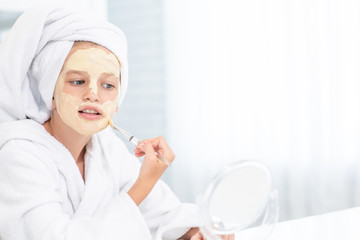 Young girl in towel on her head  make a clay facial mask at home. Empty space for text