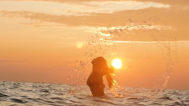 silhouette of a woman tumbling out of the water making a circle with hair with splashes of drops at dawn, a girl swimming in the sea enjoying sunrise, summer vacation concept