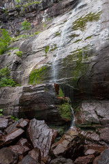 Low angle view of almost dried up waterfall during summer and shiny, wet, red rocks of vertical cliff covered by green moss