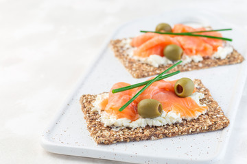 Sandwich with smoked salmon and cream cheese on thin multi seed  crispbread, garnished with green onion and olives, horizontal, copy space.