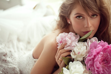 Beautiful bride posing in lightfull white room among peonies flowers. - Image