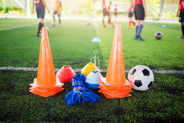 Soccer ball and marker cone with training equipment on green artificial turf with blurry player...
