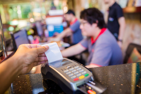 Hand put credit card In slot of credit card reader with blurry cashier and customer at counter service, credit card payment, buy and sell products & service, the concept of payment, selective focus.