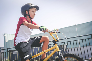 Portrait of a young cyclist with bmx ready to start. Young boy wearing helmet riding a bicycle looking the race track. A child having fun outdoor in the park. Safety, competition, youth sport, concept