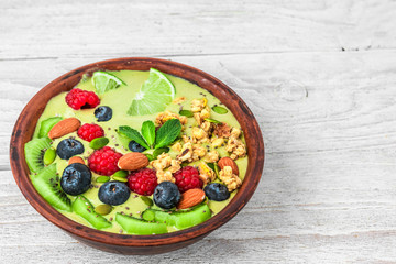 green smoothie bowl made of matcha tea with fresh fruits, berries, nuts, seeds for healthy vegan diet breakfast