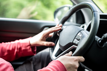 Man hand holding car steering wheel - Male hand close up shallow dof depth of field driving car - Two hands on steering wheel in traffic driving style background backdrop focus on steering wheel