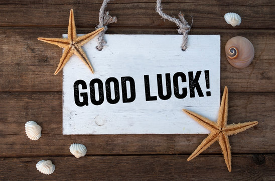 White wooden board on brown weathered wood with words Good Luck and maritime decoration