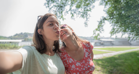 Girlfriends taking selfie together having fun outdoors concept of modern women friendship lifestyle best friends happy girls travel on break or city vacation bright warm day laughing cheerful kiss