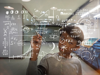 Young Asian boy writing mathematical and physic formula onto a clear glass. Selected focus