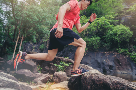 Crop Image of sport running man in cross country trail run jumping on the rocky mountain path.