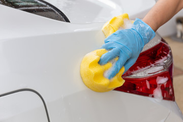 Woman hand wearing blue gloves with yellow sponge washing taillight modern car or cleaning automobile. Car wash concept