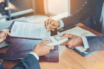Fototapeta na wymiar Crop image of businessman puts signature on contract at business meeting and passing money after negotiations with business partners