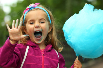 Closeup portrait of happy toddler girl eating bright blue cotton candy