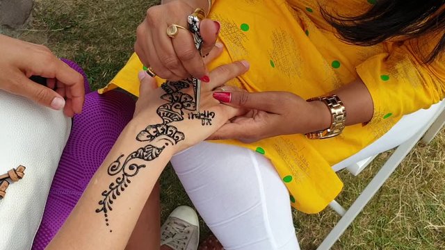 Indian girl draws mehendi henna pattern on her hand.