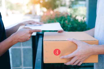 Young asian man smiling while delivering a cardboard box to the woman holding document to signing signature.