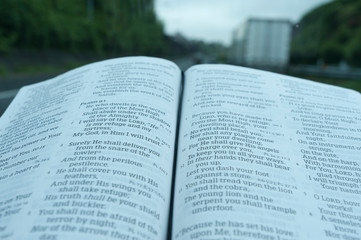 Close up of open Holy Bible in Psalm 91. Windshield with raindrops. Blurred background with...