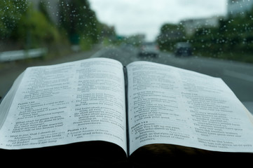 Open Holy Bible in Psalm 121 in rainy day. Blurred background with expressway and cars. Horizontal...
