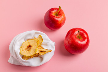 Homemade sun-dried organic apple slices, crispy apple chips, on pink background with fresh apple.