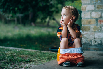 little child sits on a  near a brick wall and looks towards the garden