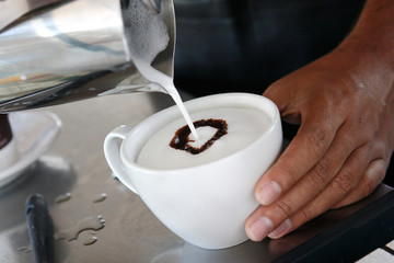 The hands of a barista prepares espresso and American coffee in a coffee mill. A cappuccino is an espresso-based coffee drink and is traditionally prepared with steam milk foam.