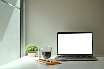 Mockup laptop computer, coffee, notebook and pen with coffee near windows.