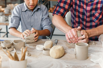 Cute caucasian boy making part of pots while his father kneading clay.