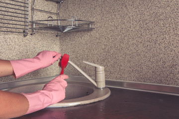 A young woman in yellow gloves washes dishes with a sponge in the sink. House professional cleaning service.