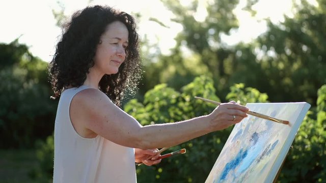 female artist painting a colorful painting outdoors in the garden