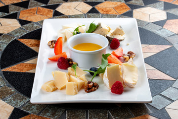 Cheese plate served with various cheese, fruits, nuts and honey on stone table