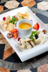 Cheese plate served with various cheese, fruits, nuts and honey on stone table