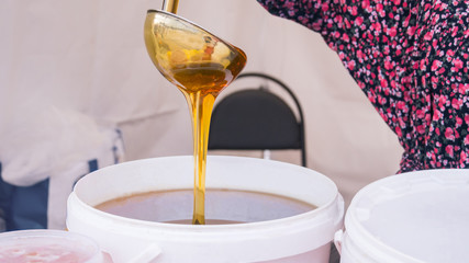 Woman pouring sweet honey from the ladle at street farmers market