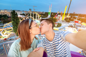 Loving mixed race couple hugging and riding on the Ferris wheel and take a selfie photo during the...