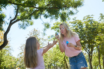 mom and daughter blow bubbles in the park