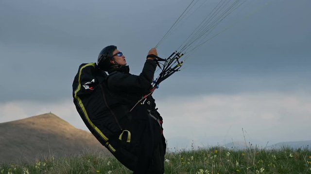 A male athlete paraglider raises a wing in an outdor against the backdrop of evening clouds but cannot fly. Failure while trying to take off