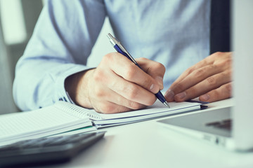 Businessman hand writing note on a notebook. Business man working at office desk. Close up of empty notebook on a blackboard with office supplies.