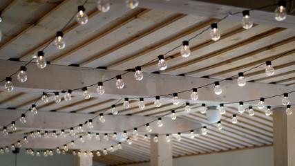 Warm color string light bulbs pending on a wooden rustic ceiling