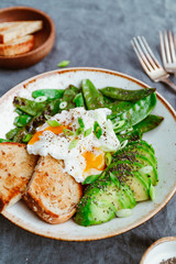 Fototapeta na wymiar Healthy breakfast or lunch. Fried snow peas, avocado, poached eggs are sprinkled chia seeds with bread toasts.
