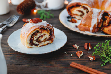 Piece of Swedish tea ring Christmas cake with cinnamon, pecans and raisins on a warm knitted sweater. The concept of cozy winter Holidays and homemade bakery.