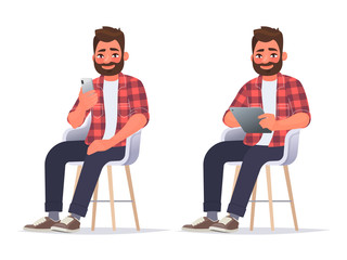 Man uses a smartphone and a tablet while sitting on a chair. Internet surfing or reading an article