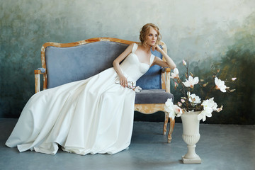 Bride in a chic long dress lying on the sofa couch. White wedding dress on the bride's body....