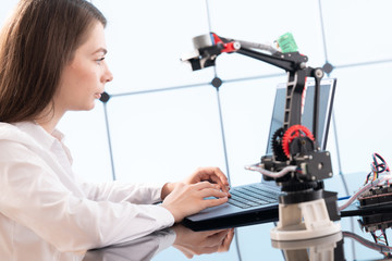 A young woman writes an algorithm for the robot arm. Science Research Laboratory for Robotic Arm...