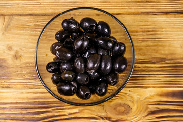 Pickled black olives in glass bowl on wooden table