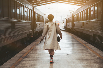 Rear view of a walking African woman in a white cloak on the railway station before her trip...